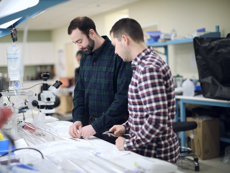 Three engineers reviewing a molded medical device component and technical drawings at a manufacturing workbench.