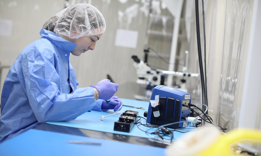 Gowned technician assembling medical device components at a cleanroom bench