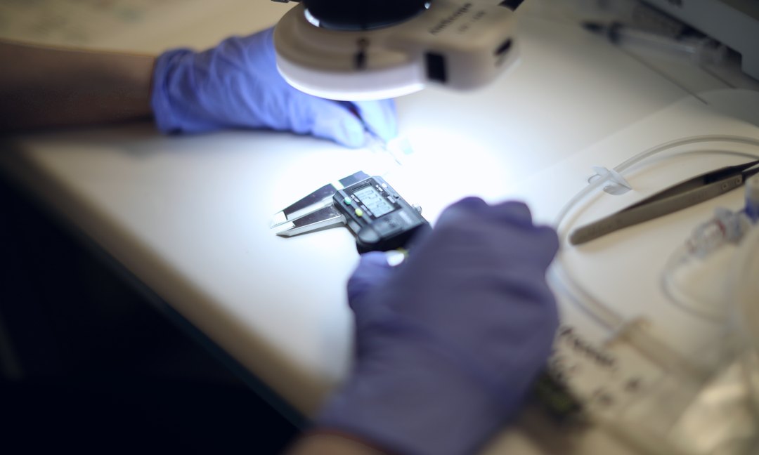 Gloved hands handling a precision component under bright inspection light