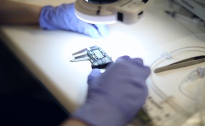Gloved hands measuring a micro-molded part with calipers