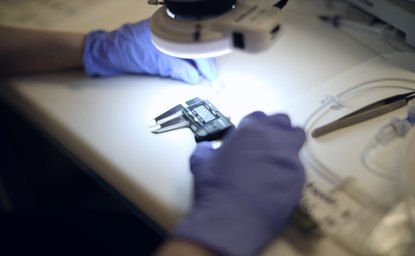 Gloved hands checking a small precision component under inspection light